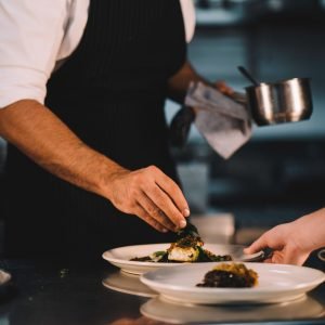 Close-up of a male chef decorating food in ceramic dishes over stainless steel worktop in restaurant kitchen.